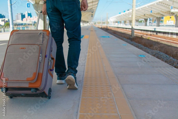 Obraz 鉄道のプラットフォームをスーツケースをひきながら歩くジーンズ姿の男性