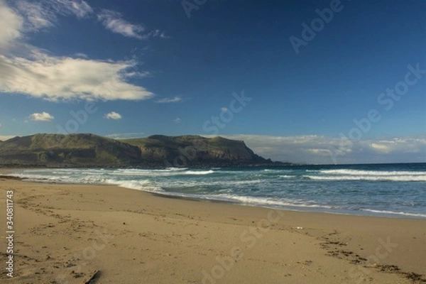 Fototapeta evocative image of sandy beach with rough sea headland in the background and clouds