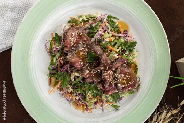 Fototapeta Asian cabbage salad with roast beef and sesame seeds on wooden table