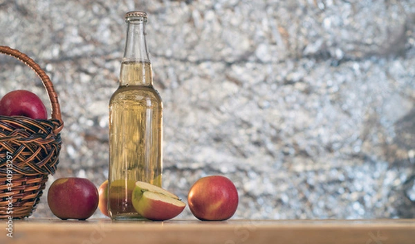 Fototapeta Basket with red fresh apples and a bottle of cider on a wooden table.