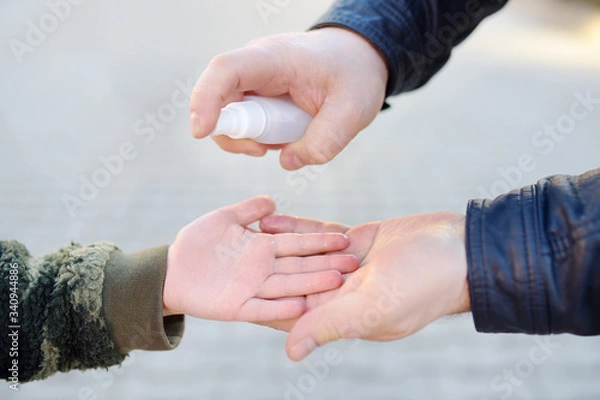 Fototapeta Mature man and little child makes disinfection of hands with sanitizer in airport, supermarket or other public place. Safety during COVID-19 outbreak.