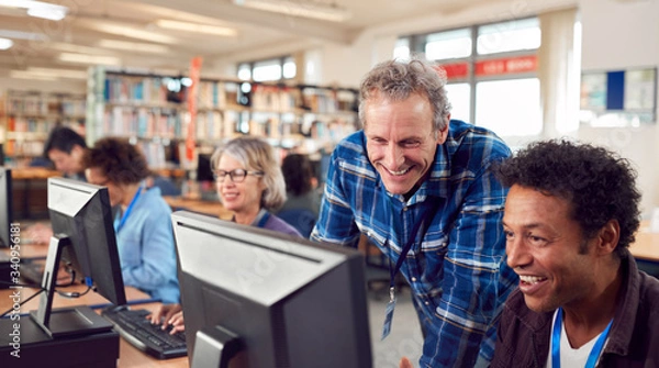 Fototapeta Teacher With Group Of Mature Adult Students In Class Working At Computers In College Library