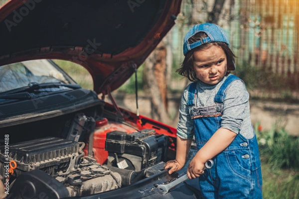 Fototapeta Little child trying to fix broken real car. Dreaming to be auto technician