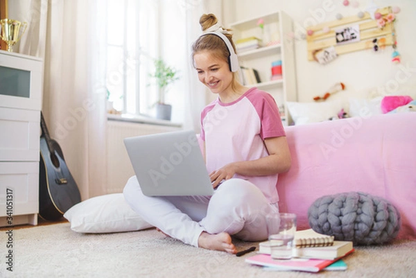 Obraz Young girl with laptop sitting on floor, relaxing during quarantine.