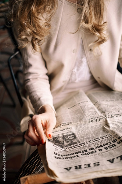 Fototapeta Girl in coat is reading a newspaper while resting in a cafe outdoors