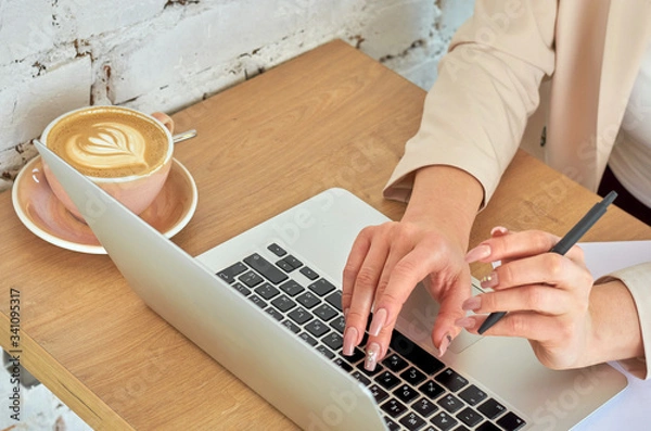 Fototapeta Female young hands with pale pink manicure are typing on a laptop keyboard.
