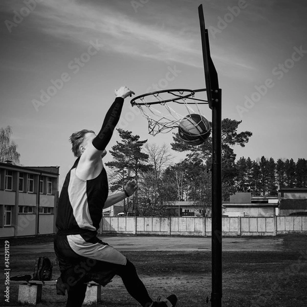 Fototapeta Young man jumping and making a slam dunk playing streetball. Black and white