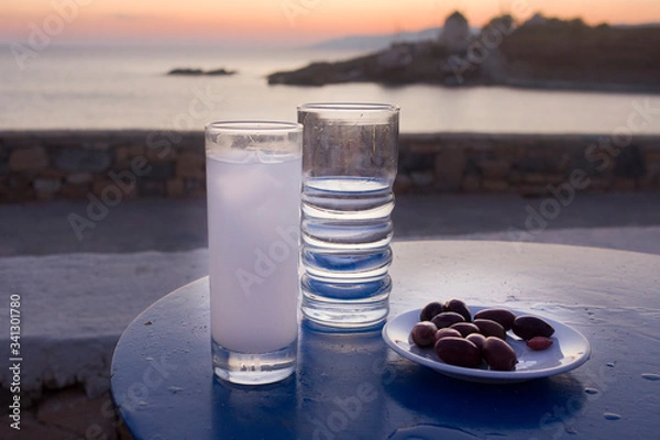Fototapeta Ouzo glass with ice, water and olives meze on sea after the sunset background. Taken in Koufonissia island,  Lesser Cyclades, Greece
