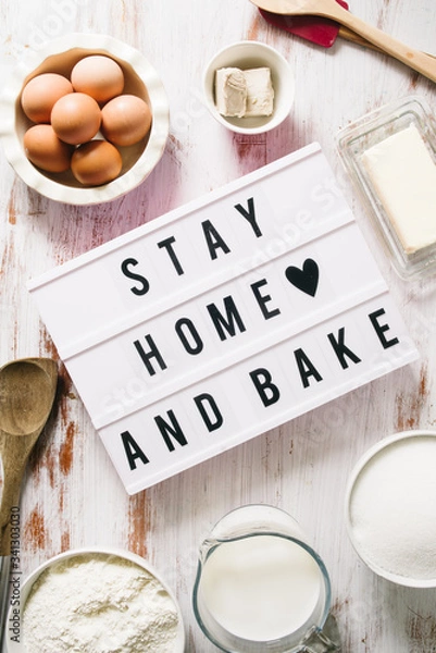 Fototapeta Stay home and bake covid 19 conceptual image for coronavirus pandemia,  with a lightbox texting stay home and bake,circled by tools and ingredients for baking bread and cake during quarantine,top view