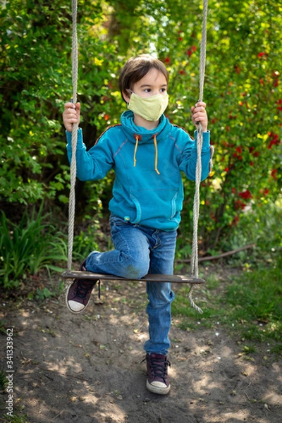 Obraz Child with face mask is sitting on a swing