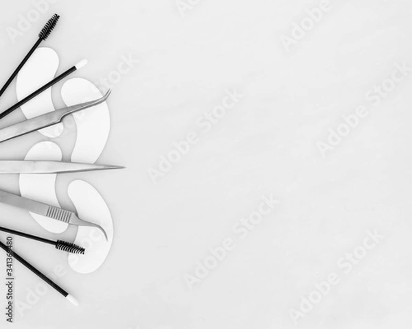Fototapeta A beauty background design with eyelash extension tweezers, gel eye pads, applicators and mascara wands laid out on the left side of the frame against a white background space for copy text