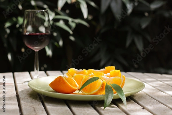 Obraz Red wine served outside in garden on white table with fresh orange in sun lights close up