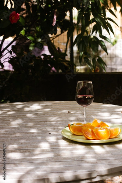 Obraz Red wine served outside in garden on white table with fresh orange in sun lights close up