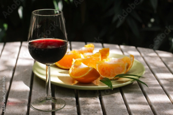 Obraz Red wine served outside in garden on white table with fresh orange in sun lights close up