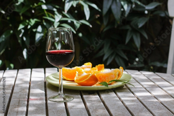 Obraz Red wine served outside in garden on white table with fresh orange in sun lights close up