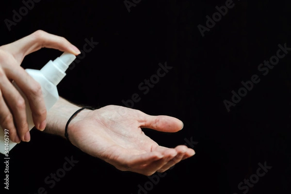 Fototapeta Male hand with a sanitizer spray disinfect his hand in the house on a black background. Covid-19 Coronavirus Quarantine Pandemic. Isolation at home. Protect yourself and your loved ones.