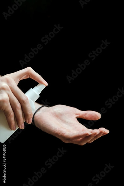 Fototapeta Male hand with a sanitizer spray disinfect his hand in the house on a black background. Covid-19 Coronavirus Quarantine Pandemic. Isolation at home. Protect yourself and your loved ones.