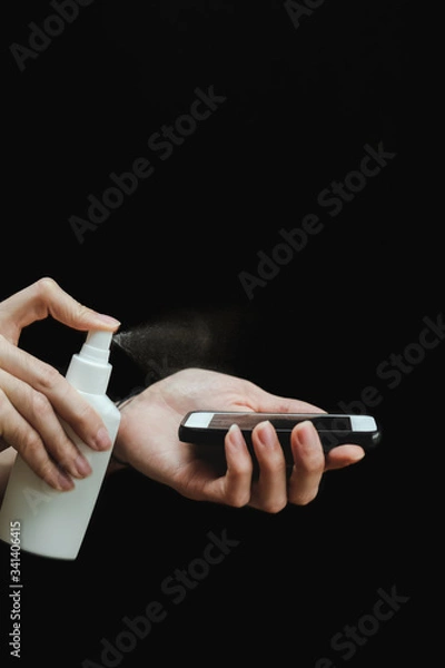 Fototapeta Male hand with a sanitizer spray disinfect the surface of the smartphone on black background. Covid-19 Coronavirus Quarantine Pandemic. Isolation at home. Protect yourself and your loved ones.