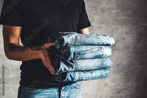 Fototapeta close up stack of folded denim blue jeans in hand over gray wall background, copy space