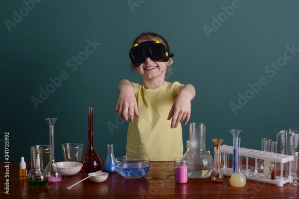 Fototapeta girl in safety glasses at home doing experiments with chemicals. school experiments at home.