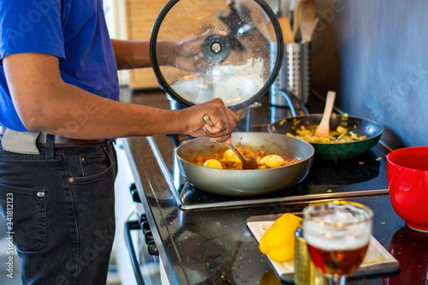 Fototapeta Man cooking and making a mess on an electric stove in the kitchen while drinking a beer. Preparing food. Messy kitchen counter