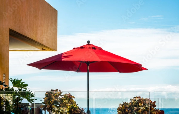 Fototapeta Red umbrella on a rooftop patio, tropical sky with an ocean view on horizon