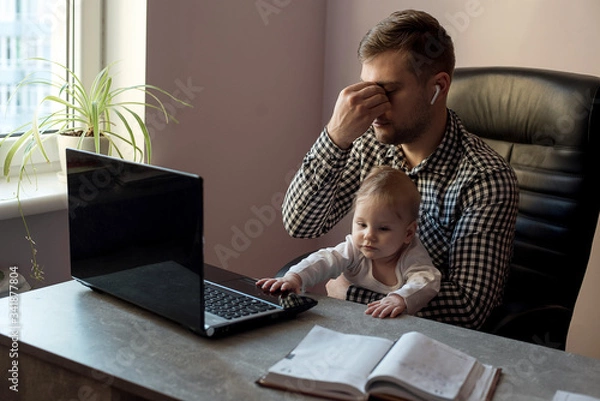 Fototapeta Young sad depressed working father work at home office while babysitting his playful baby daughter at home.Negative emotion concept