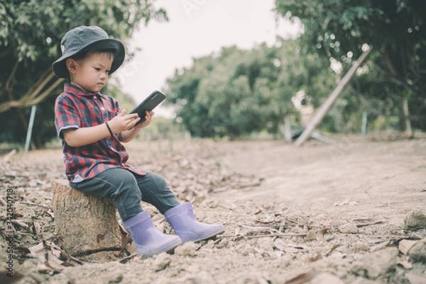 Obraz A cute little farmer in Asia wears a red shirt working through a mobile phone. The concept of agribusiness