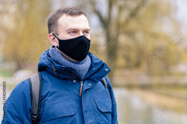 Fototapeta Portrait of a handsome man with blue eyes in a black protective mask during the  Covid virus quarantine period