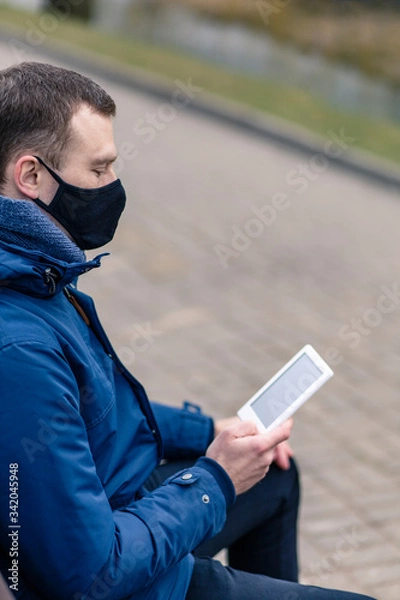 Fototapeta Protective mask on a person's face. A man reads a book in the street.