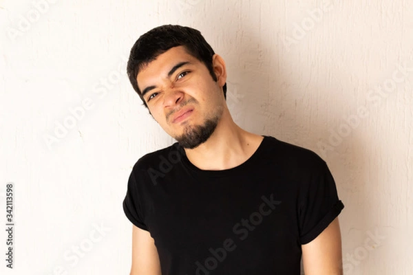 Obraz Young short-haired Hispanic man with black clothes, angry, furious, upset, stressed posing on a white background