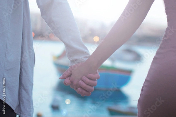 Fototapeta close up of couple holding hands, having date walking in Malta with traditional boat on background,love concept