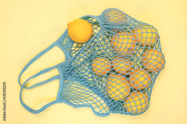 Fototapeta A lot of yellow lemon in the blue mesh bag flat lay on yellow background. Zero waste, eco friendly, no plastic concept. Citrus fruits.