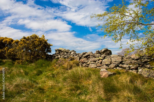 Fototapeta An old wall on the top of a fell with blue sky and clouds.