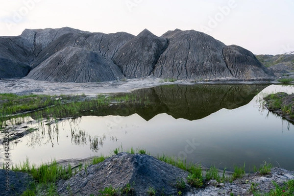 Fototapeta Lake in a coal pit with clear water at sunset. Reflection in the water of a coal mountain, hill, trees, reeds.The fuel industry produces coal in an open way.