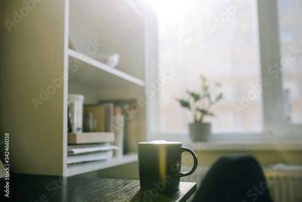 Fototapeta Cup with coffee on table near shelves on window background