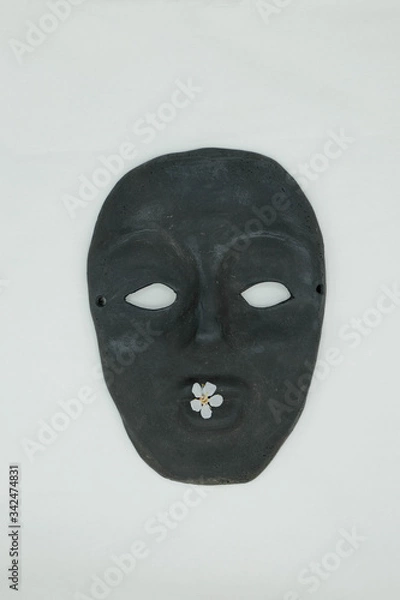 Fototapeta  Black ceramic mask on a white background. White flower on lips mask. Mass produced mask. Copy space.