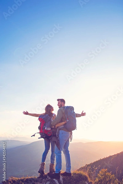 Fototapeta Hikers with backpacks relaxing on top of a mountain and enjoying the view of valley
