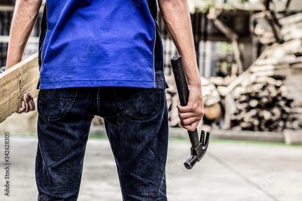 Fototapeta A carpenter holding his back with a hammer and a piece of wood standing back with a space for text.