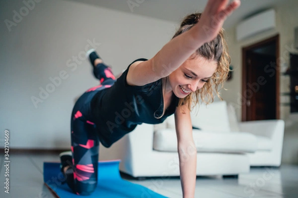 Fototapeta giovane bella ragazza fa sport a casa eseguendo esercizi a corpo libero. Smart gym e distanza sociale durante la pandemia 