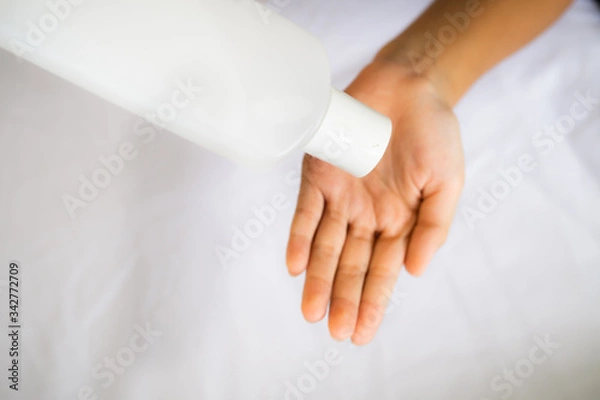 Fototapeta Hand applying sanitizer from the bottle on a white background.