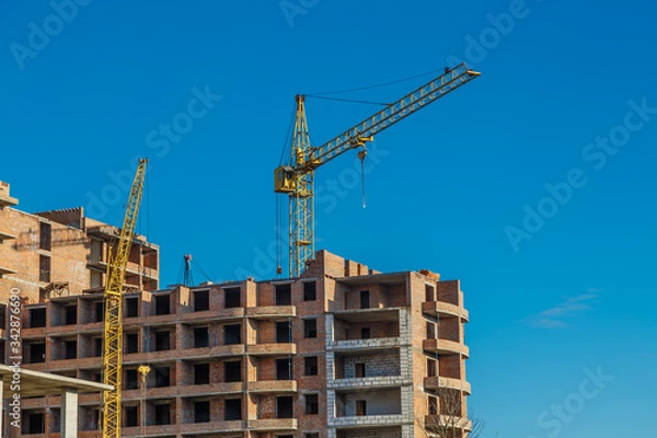 Fototapeta Extensive scaffolding providing platforms for work in progress on a new apartment block,Tall building under construction with scaffolds,Freestanding tower crane on a building site