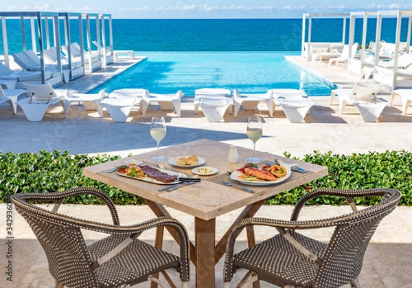 Obraz Oceanfront restaurant table, pool and ocean background, food and drinks, bread and butter