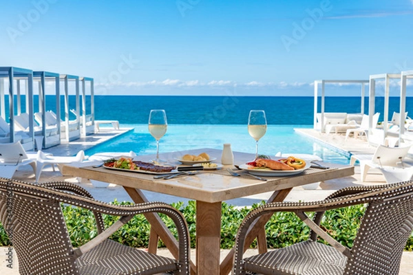 Obraz Oceanfront restaurant table, pool and ocean background, food and drinks, bread and butter