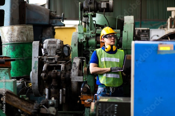 Fototapeta Portrait Engineer man working with computer laptop or tablet at factory Equipment. Chief Engineer in the Hard Hat Holds Laptop at the industrial facility.