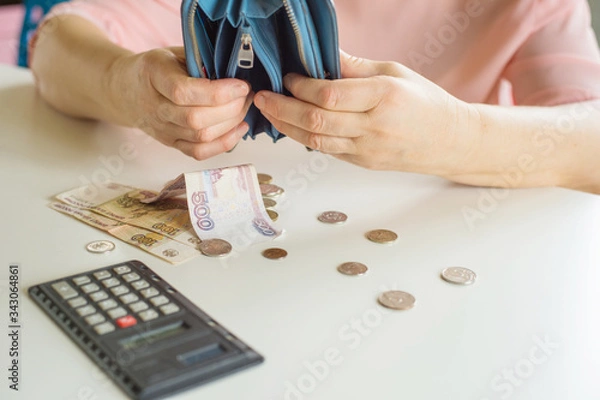 Fototapeta close-up of a woman's hand shakes out a bare wallet on a table Russian money rubles coins on a white table background place for text topic of the financial crisis