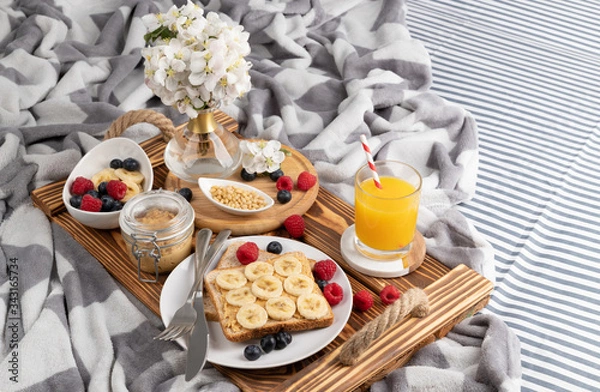 Fototapeta Breakfast in bed. Wooden tray with glass of orange juice and sandwich with berries