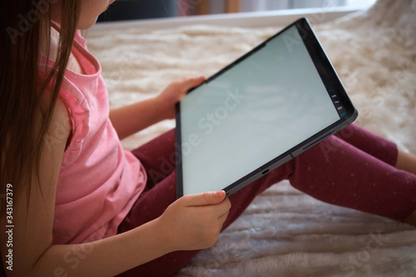 Obraz A child with a tablet sits on the bed. distance learning. Games and activities for children