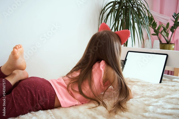 Obraz A child with a tablet sits on the bed. distance learning. Games and activities for children