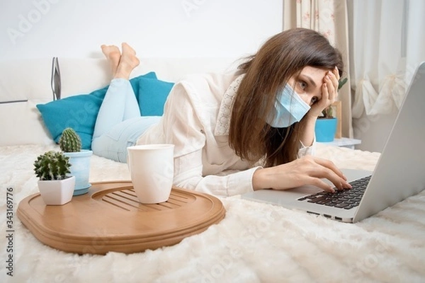 Obraz Work from home at the quarantine.Sick woman in nose guard runs business from home. Remote work on the internet during sick leave or self isolation